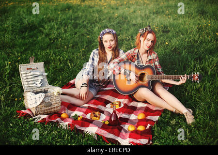 Zwei glückliche Mädchen Kleidung im Pin-up-Stil auf Picknick, Gitarre spielen, lecker Essen, Spaß haben. Selektiven Fokus. Bild t Stockfoto