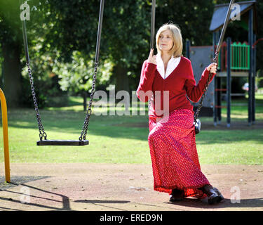 Eine Frau in rot saß auf einer Schaukel in einem Park. Stockfoto