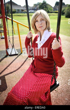 Eine Frau in rot saß auf einer Schaukel in einem Park. Stockfoto