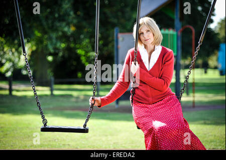 Eine Frau in rot saß auf einer Schaukel in einem Park. Stockfoto