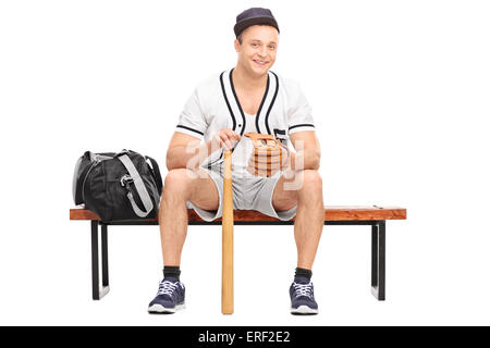 Junge Baseballspieler mit einem Baseballhandschuh und eine Fledermaus auf der Bank sitzen und schaut in die Kamera, die isoliert auf weißem Hintergrund Stockfoto