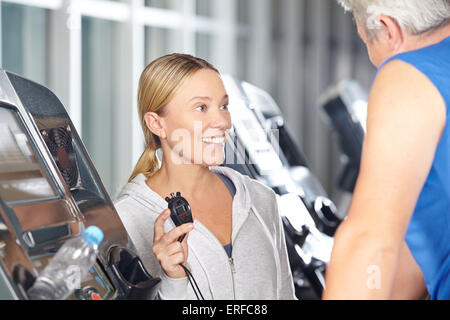 Trainer mit Stoppuhr in einem Fitness-Center im Gespräch mit Senior auf Laufband Stockfoto