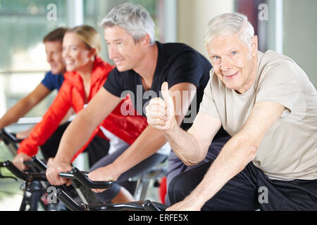 Happy senior woman im Fitnessstudio am spinning Bike seine Daumen hochhalten Stockfoto