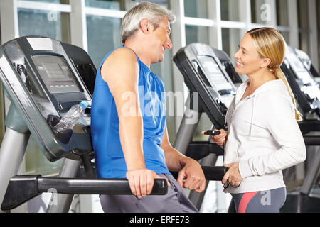 Zwei glückliche Senioren im Fitness-Center auf einem Laufband im Gespräch Stockfoto