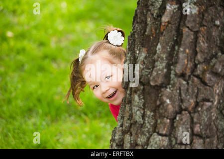 niedliche kleine Mädchen versteckt sich hinter riesigen Baum. Kinder Porträt Blick in die Kamera Stockfoto
