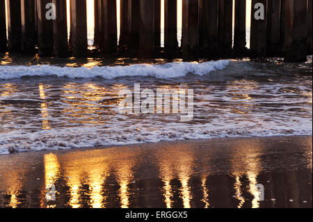 Golden Reflexion der Sonne und konkrete Säulen der Pier auf nassen Strand Sand waschen wo Wellen gegen die Küste sind Stockfoto