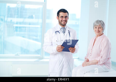 Arzt mit Zwischenablage und Patient Blick in die Kamera Lächeln Stockfoto