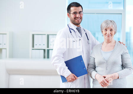 Lächelnde Arzt mit Zwischenablage und ältere Patientin in Klinik Stockfoto