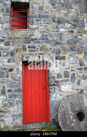 Wunderschönes altes Steingebäude mit leuchtend roten Holztüren und Fenstern, antiker Schleifstein vor dem Gebäude. Stockfoto