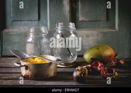 Mango-Chutney oder Marmelade in Vintage Aluminium über alte Tabelle mit leeren Glas, Mango und Mangosteen pan machen. Dunkel rustikalen atmos Stockfoto