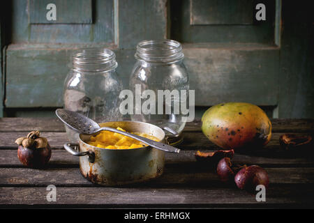 Mango-Chutney oder Marmelade in Vintage Aluminium über alte Tabelle mit leeren Glas, Mango und Mangosteen pan machen. Dunkel rustikalen atmos Stockfoto