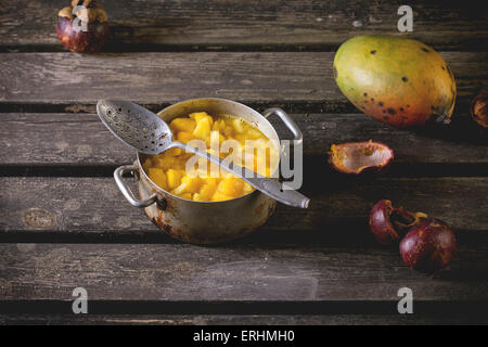 Mango-Chutney oder Marmelade in Vintage Aluminium über alte Tabelle mit Mango und Mangosteen pan machen. Dunkle, rustikale Atmosphäre Stockfoto