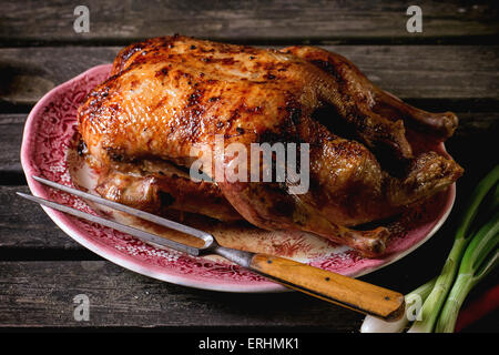 Ganze gebratene Honig Ente mit Fleischgabel in Vintage Platte, über alten Holztisch serviert. Stockfoto