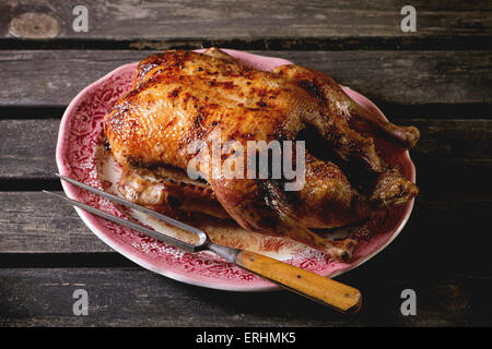 Ganze gebratene Honig Ente mit Fleischgabel in Vintage Platte, über alten Holztisch serviert. Stockfoto