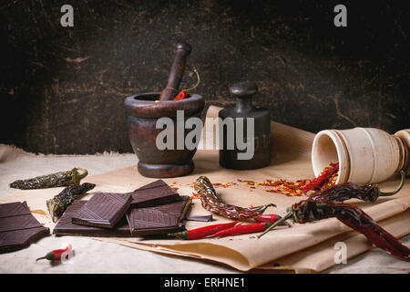 Dunklen Schokolade mit frische und trockene rote scharfe Chilischoten auf Backpapier mit Vintage hölzerne Mörser und Gewicht über dunkel hacken Stockfoto