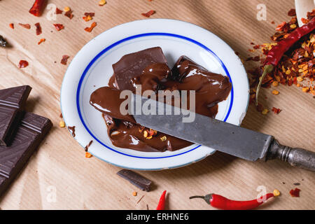 Dunklen Schokolade mit frische und trockene rote scharfe Chilischoten auf Backpapier mit Teller heiße geschmolzene Schokolade und Vintage hacken Stockfoto