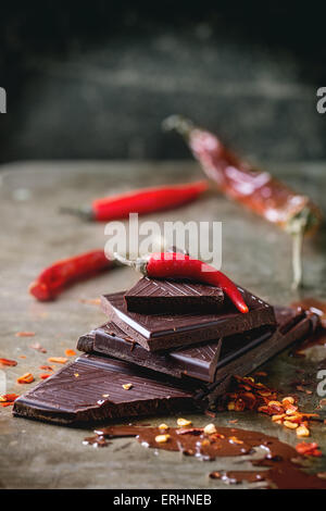 Hacken und Schmelzen von dunkler Schokolade mit frischen und trockenen roten hot Chili Peppers über alte Metall Hintergrund. Selektiven Fokus. Stockfoto