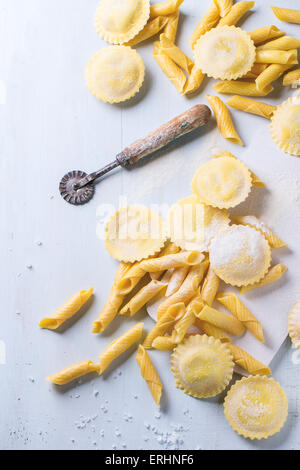 Hausgemachte Ravioli und Garganelli Nudeln mit Mehl und hölzerne Walze über hölzerne hellblauen Hintergrund. Ansicht von oben Stockfoto