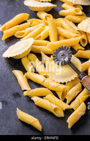 Hausgemachte Ravioli und Garganelli Nudeln mit Mehl und hölzerne Walze über schwarzem Schiefer. Stockfoto