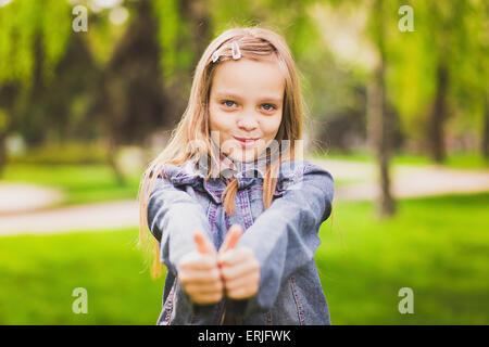 Junges Mädchen legt ihren Daumen. Porträt von fröhlichen Kind. Lächelndes Mädchen Spaß außerhalb. Erfolgreiche glücklich. Stockfoto