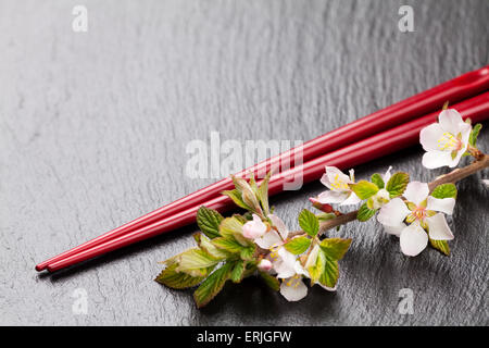 Japanische Sushi-Stäbchen und Sakura Blüte auf schwarzem Stein. Draufsicht mit Textfreiraum Stockfoto