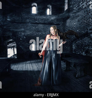 junge schöne weibliche Vampir Aristokrat mit einer Tasse Blut steht in der alten Burg Stockfoto