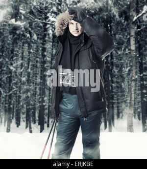 Junger Mann Skifahrer trägt schwarzes Fell Kapuze Winterjacke und hält Stöcke im Winterwald Stockfoto