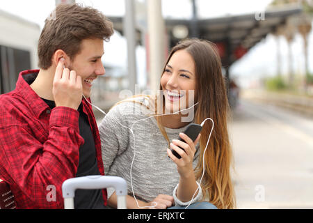 Glückliches Paar von Reisenden austauschen von Musik auf Urlaub während einer Reise in einem Bahnhof Stockfoto