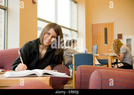 Junge Erwachsene weibliche College-Student studieren gemeinsam mit Lehrbuch lächelt in die Kamera. Stockfoto