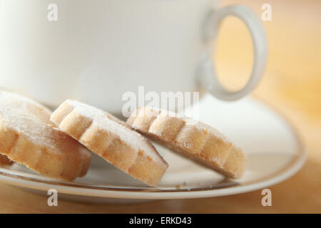 Italienische Butterkekse auf einer weißen Tasse eine Untertasse. Diese Cookies haben eine Blütenform und sind mit Puderzucker bestreut Stockfoto