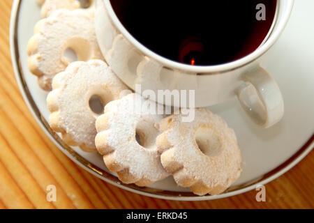 Italienische Butterkekse auf eine Untertasse eine Tasse schwarzen Tee. Diese Cookies haben eine Gänseblümchen-Form und sind bestreut mit Puderzucker suga Stockfoto