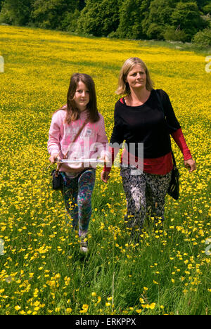 Mutter und 9 Jahre alte Tochter, die zu Fuß durch ein Feld von Butterblumen, wie sie in einem afrikanischen Trail auf der Suche nach dem Exti teilnehmen Stockfoto