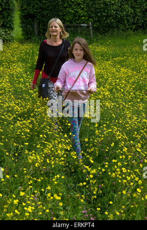 Mutter und 9 Jahre alte Tochter, die zu Fuß durch ein Feld von Butterblumen, nehmen sie Teil in einem afrikanischen Trail auf der Suche nach... Stockfoto