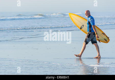 Eine senior Surfer in Jacksonville Beach, Florida betritt die menschenleere Wasser für einen Sonnenaufgang-Surf-Session. Stockfoto