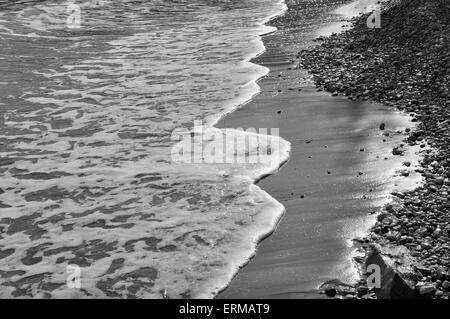 Wellen am Steinstrand Gewässer Rand abstrakte Meer Hintergrund. Schwarz und weiß. Stockfoto