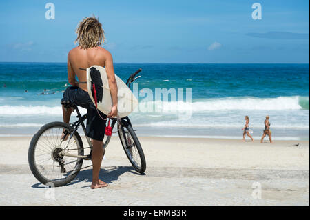 Brasilianische Surfer auf einem Fahrrad sitzen auf Fahrrad mit Blick auf die Wellen Ipanema Strand Rio de Janeiro Brasilien Stockfoto