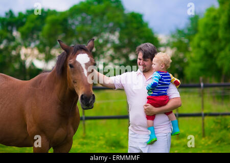 Familie auf einem Bauernhof im Sommer. Vater und Baby Sohn ein Pferd zu füttern. Outdoor-Spaß für Eltern und Kinder. Kinder spielen mit Haustieren. Stockfoto