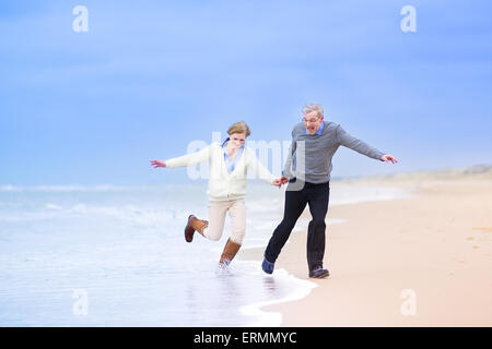 Mittleren Alter Brautpaar, schöne aktive Frau und lachende Mann läuft auf einem Strand springen weg von Wellen an der Nordsee, Stockfoto