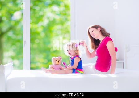 Glückliche Familie, schöne junge Mutter und ihre entzückende Tochter, süß lustig Mädchen mit dem lockigen Haar Bürsten Haare Stockfoto