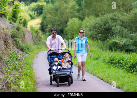 Junge Eltern Wandern in den Bergen mit Doppel Twin Kinderwagen mit zwei Kindern, Bruder und Schwester, Baby Boy und Kleinkind Mädchen Stockfoto