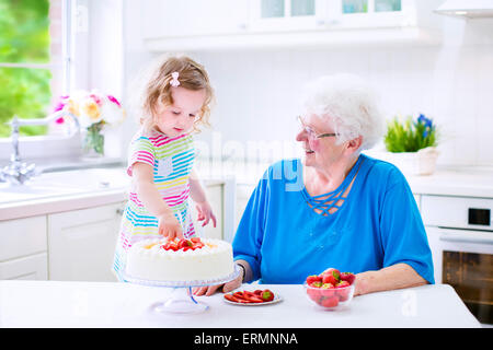 Glücklich senior Lady, liebevolle Großmutter, einen hausgemachte Erdbeerkuchen mit ihrer Enkelin in eine weiße moderne Küche Backen Stockfoto