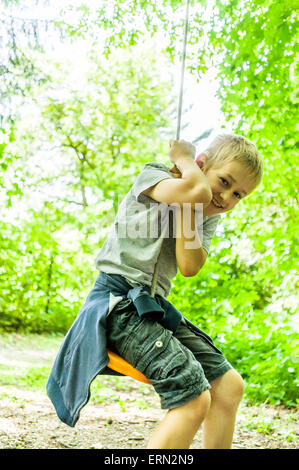 Blonde Junge an der Schaukel sitzend in Holz Stockfoto