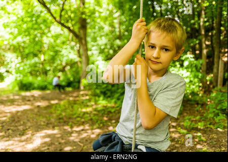 Blonde Junge an der Schaukel sitzend in Holz Stockfoto