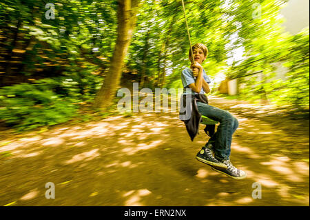 Blonde Junge an der Schaukel sitzend in Holz Stockfoto