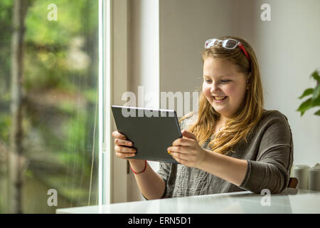 Teenager-Mädchen mit Tablet in Händen sitzt an einem Tisch am Fenster. Stockfoto