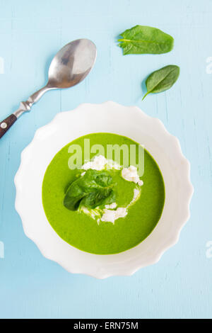 Grüne Creme Spinatsuppe mit Sauerrahm auf blauen Holztisch Stockfoto