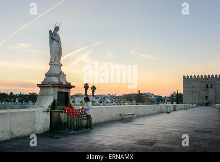 Eine Frau Licht eine Kerze in der Morgendämmerung unterhalb der Statue von Saint Raphael auf dem römischen Brücke in Cordoba Stockfoto