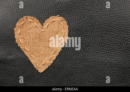 Das symbolische Herz aus Sackleinen liegt auf einem natürlichen Leder als Hintergrund Stockfoto