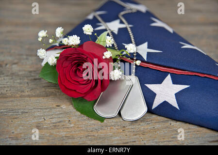 Militärische Erkennungsmarken und rote Rose mit gefalteten amerikanische Flagge auf rustikalen Holz. Stockfoto