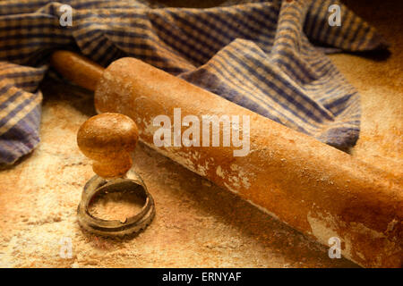 Ein antikes Nudelholz sitzt auf einer bemehlten Fläche eine Ravioli-Presse und einem karierten blauen und weißen Handtuch. Stockfoto